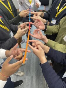 Students trying to collaboratively lift a coloured stick in a teamwork exercise